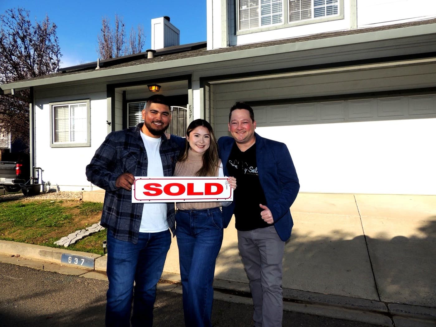 Happy clients with a SOLD sign in front of a white home with Scott Sweeney